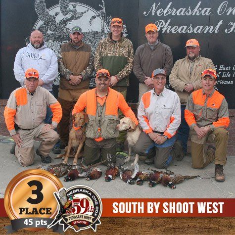 Group photo of hunters with dogs and game birds, third place winners in a Nebraska pheasant hunt.