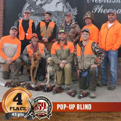 Group of hunters in orange vests with dogs and pheasants, celebrating a 4th-place win in Nebraska.