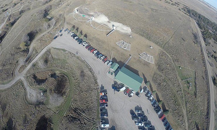 Aerial view of a parking lot filled with cars next to a green-roofed building on a hillside.