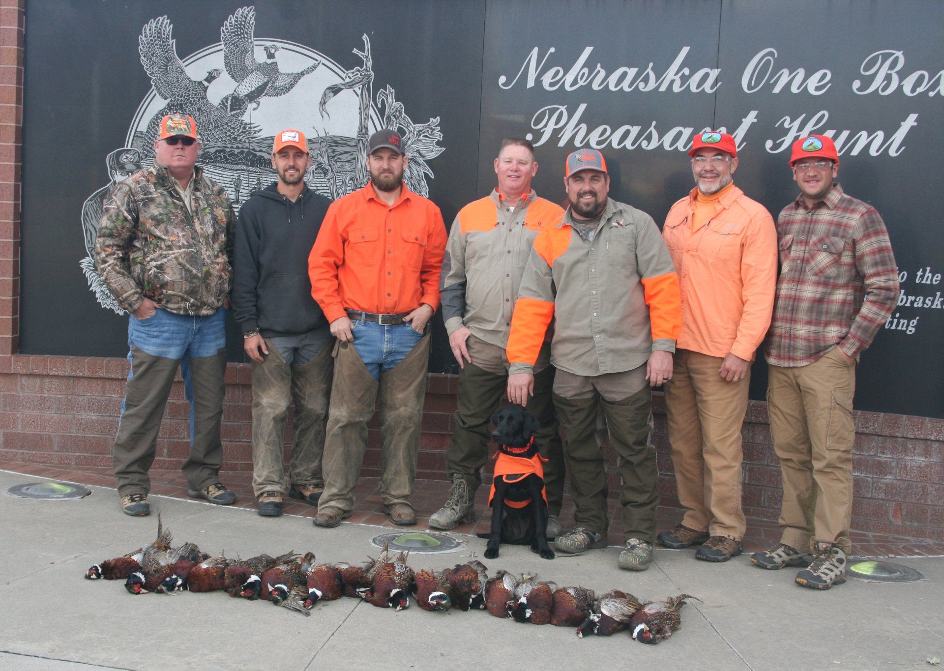 Group of hunters with their dog posing with harvested pheasants in Nebraska.