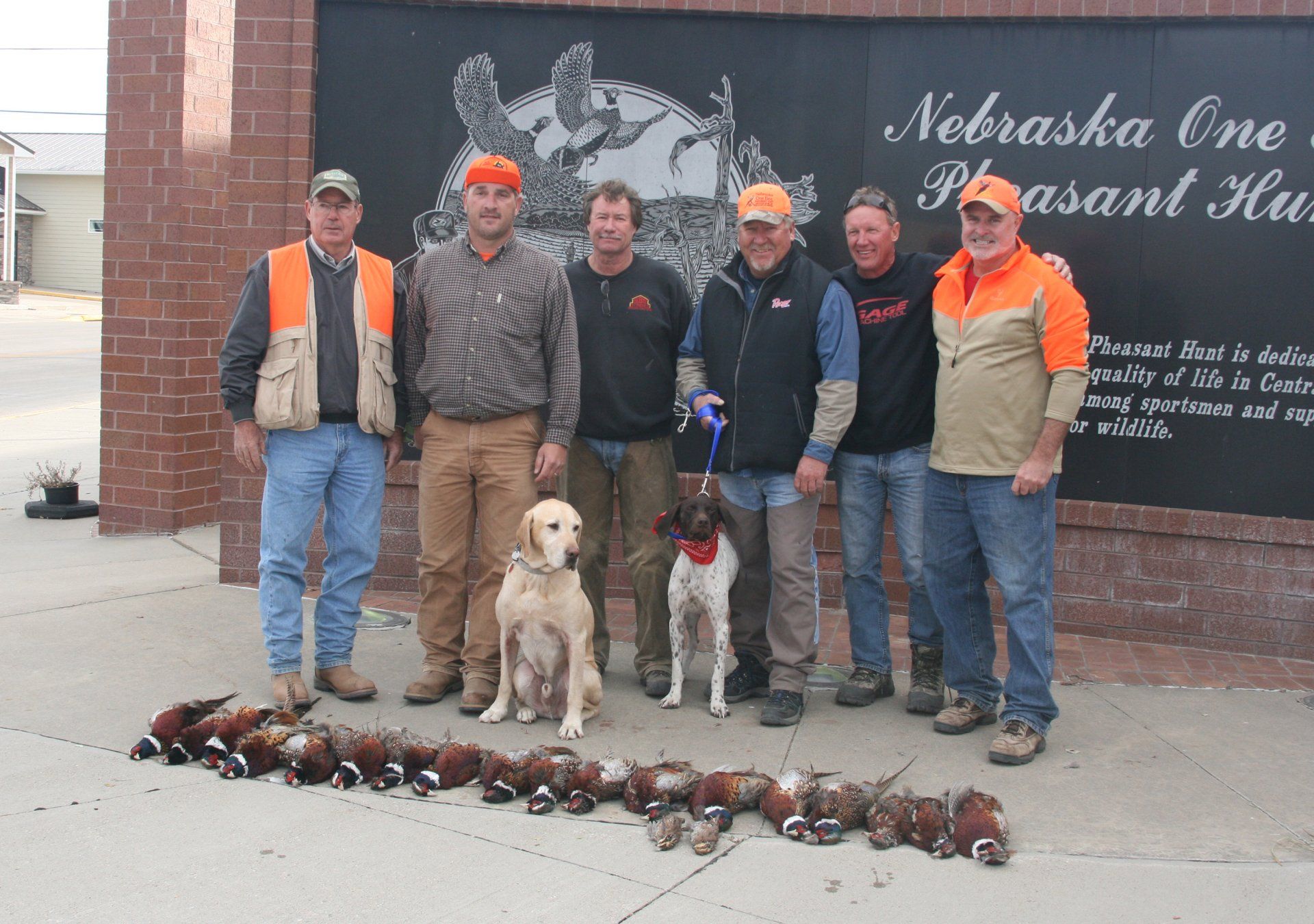 Group of hunters with two dogs pose with pheasant game in Nebraska.