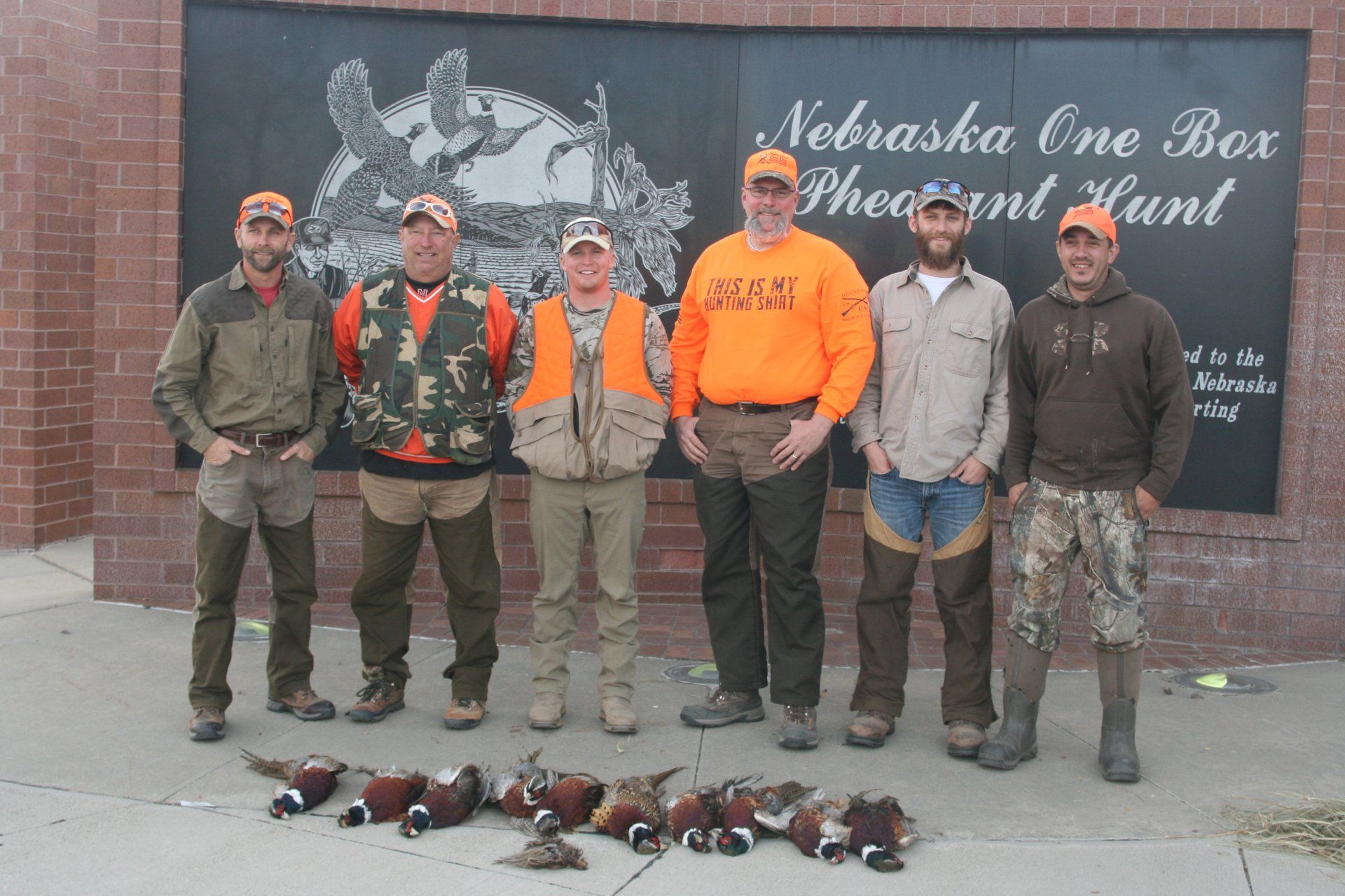 Group of hunters posing with pheasant, Nebraska One Box Pheasant Hunt. They are wearing hunting gear.