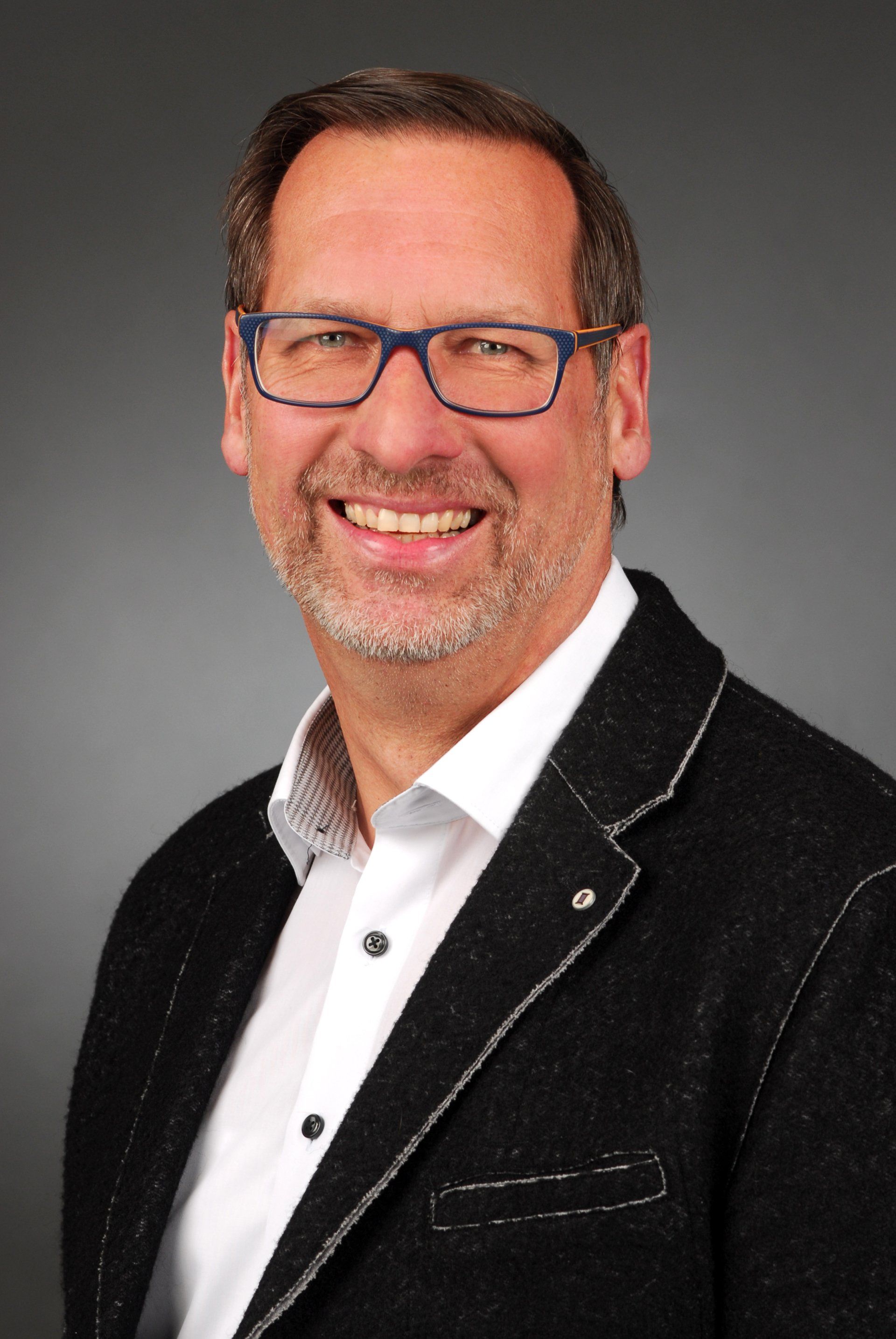 Ein Mann mit Brille und schwarzer Jacke lächelt in die Kamera.