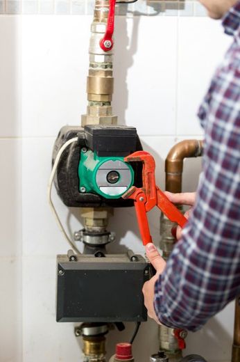 Closeup of plumber repairing heating system with red pliers - Plumbing and Heating Service in Bloomington, IL