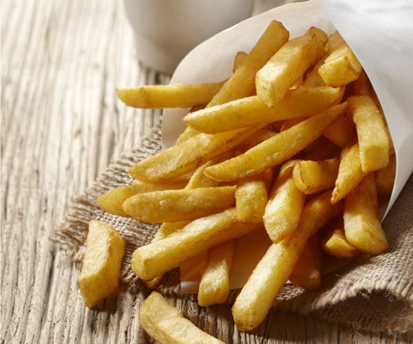 Frietjes die uit een witte papieren zak op een houten oppervlak vallen.