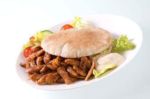 Shawarma op een wit bord met pitabrood, sla, tomaat, komkommer en saus.