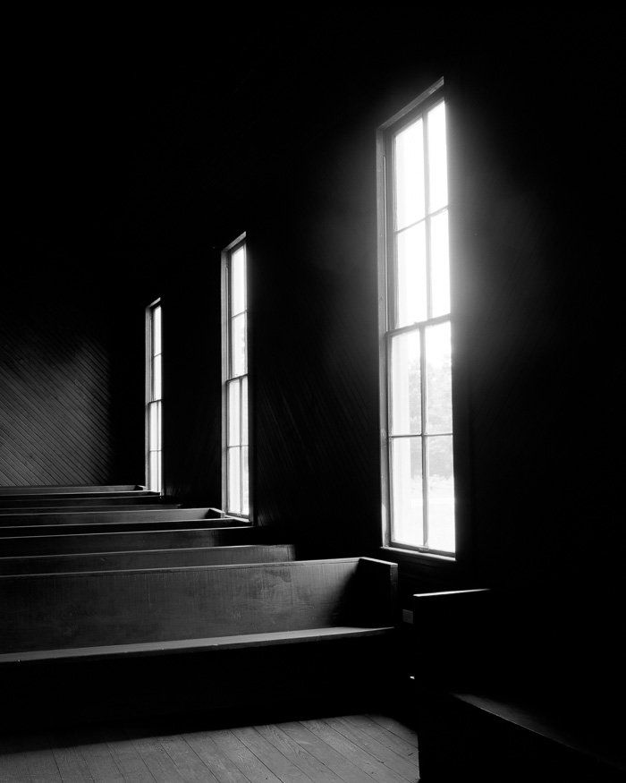 a black and white photo of a church with the sun shining through the windows