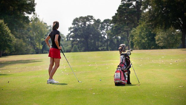 a woman is standing on a golf course with a golf club and a golf bag .