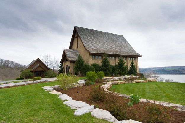 a large stone church is sitting on top of a hill next to a lake .