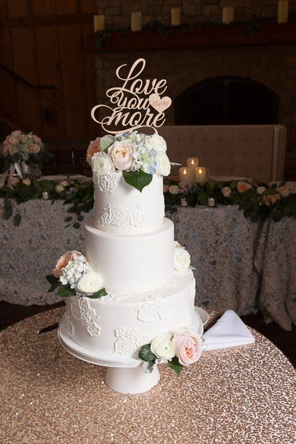a wedding cake is sitting on a table with a cake topper that says `` love you more '' .