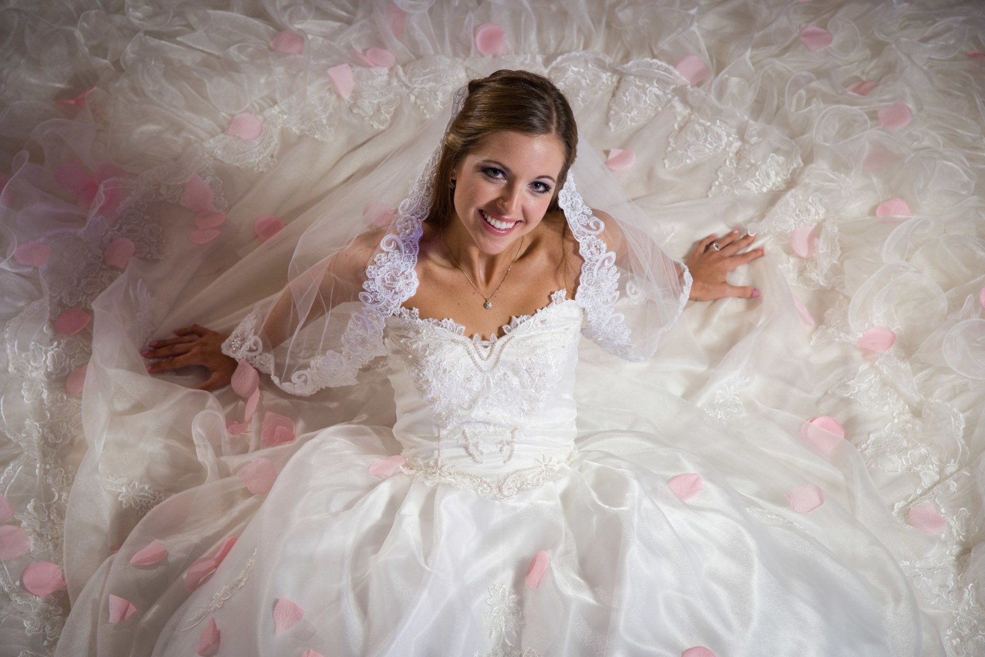a woman in a wedding dress is laying on a bed covered in pink rose petals