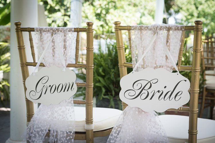 a bride and groom sign hangs from the back of their chairs