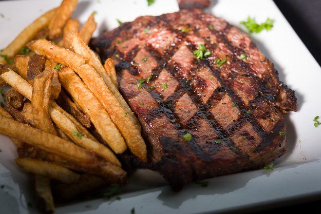 a grilled steak and french fries on a white plate .