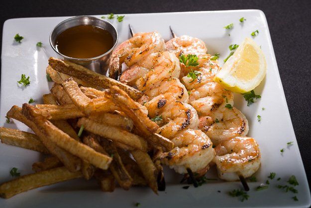 a white plate topped with grilled shrimp and french fries .