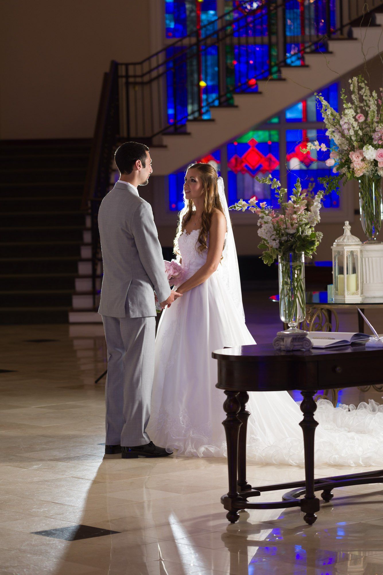 a bride and groom hold hands in front of a stained glass window