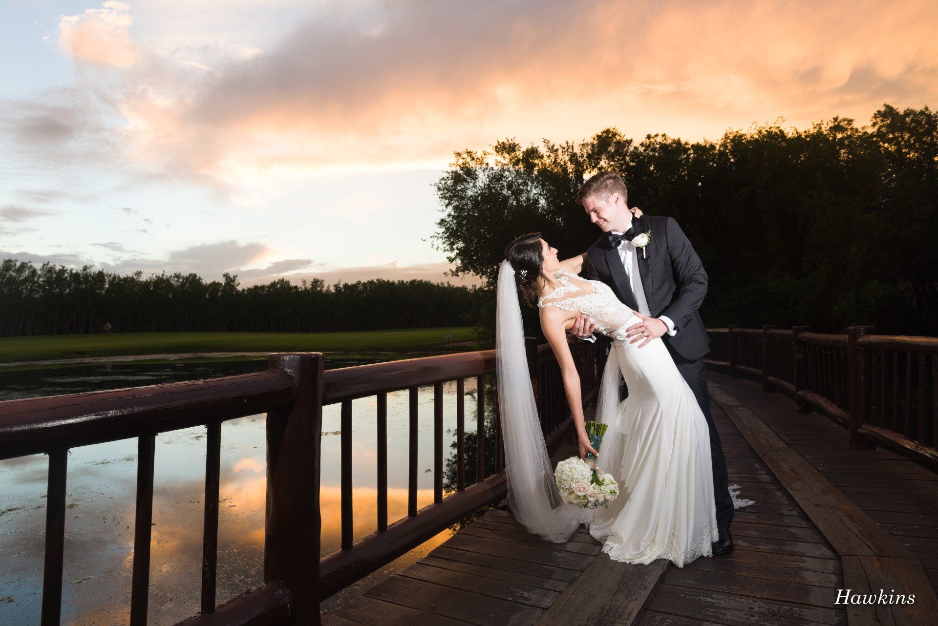 a bride and groom pose for a photo on a bridge by hawkins