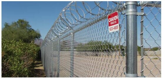 Chain-link fence with razor wire and a warning sign against a blue sky.