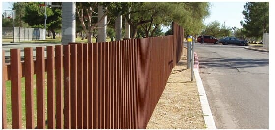 A brown wooden slat fence bordering a road with cars parked in the distance.