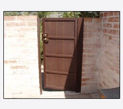 Wooden gate in a brick wall, brown door with metal hardware, sunlight casting a shadow.