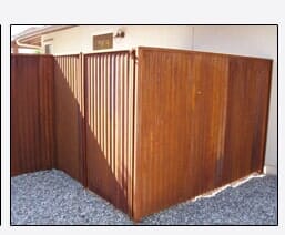 Brown wooden fence surrounding a gravel-covered area next to a building.