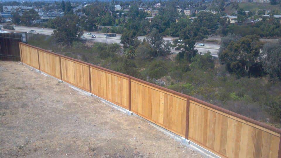 Wooden fence overlooking a green landscape with trees and a distant roadway.