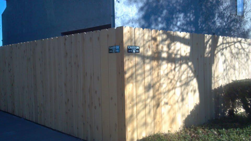 Wooden fence corner in bright sunlight, casting tree shadow, with two small black signs.