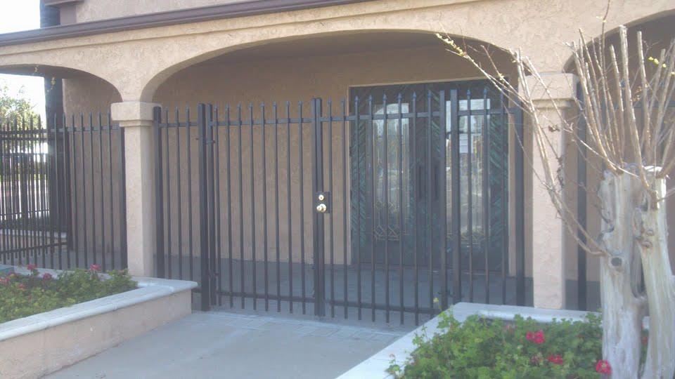 Black metal gate and fence in front of a tan building with an arched entrance.