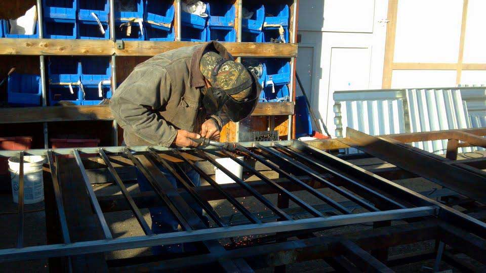 Welder in a workshop working on a metal gate, wearing a welding helmet.