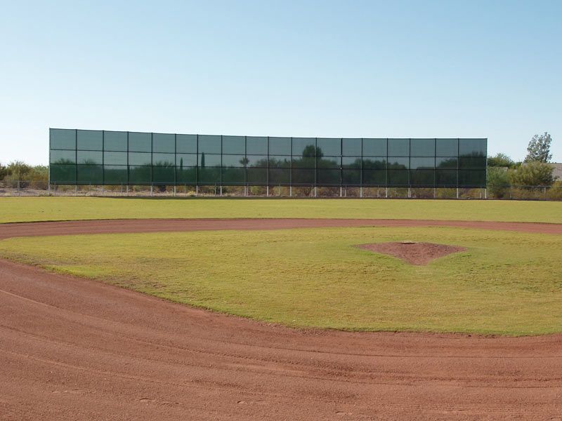 Baseball field with green grass, red dirt, and a tall, dark outfield fence.