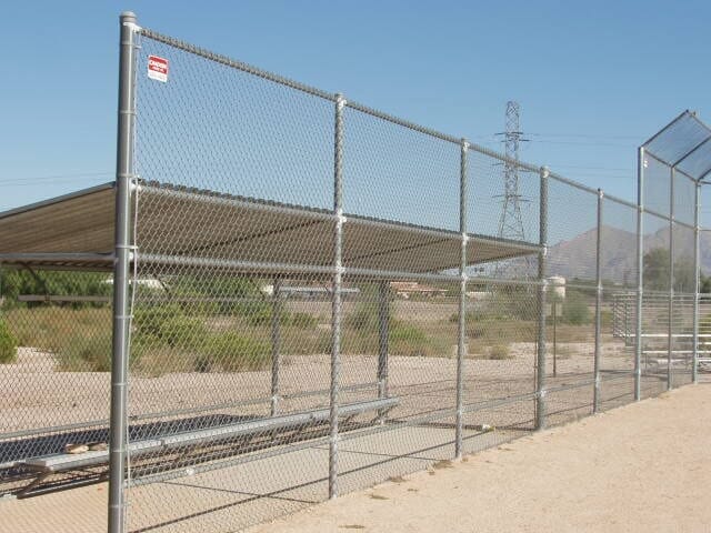 Chain-link fence surrounding a covered dugout. The shelter has a brown roof and benches.
