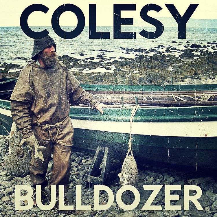 A man with a beard is standing in front of a boat with the name colesy on it