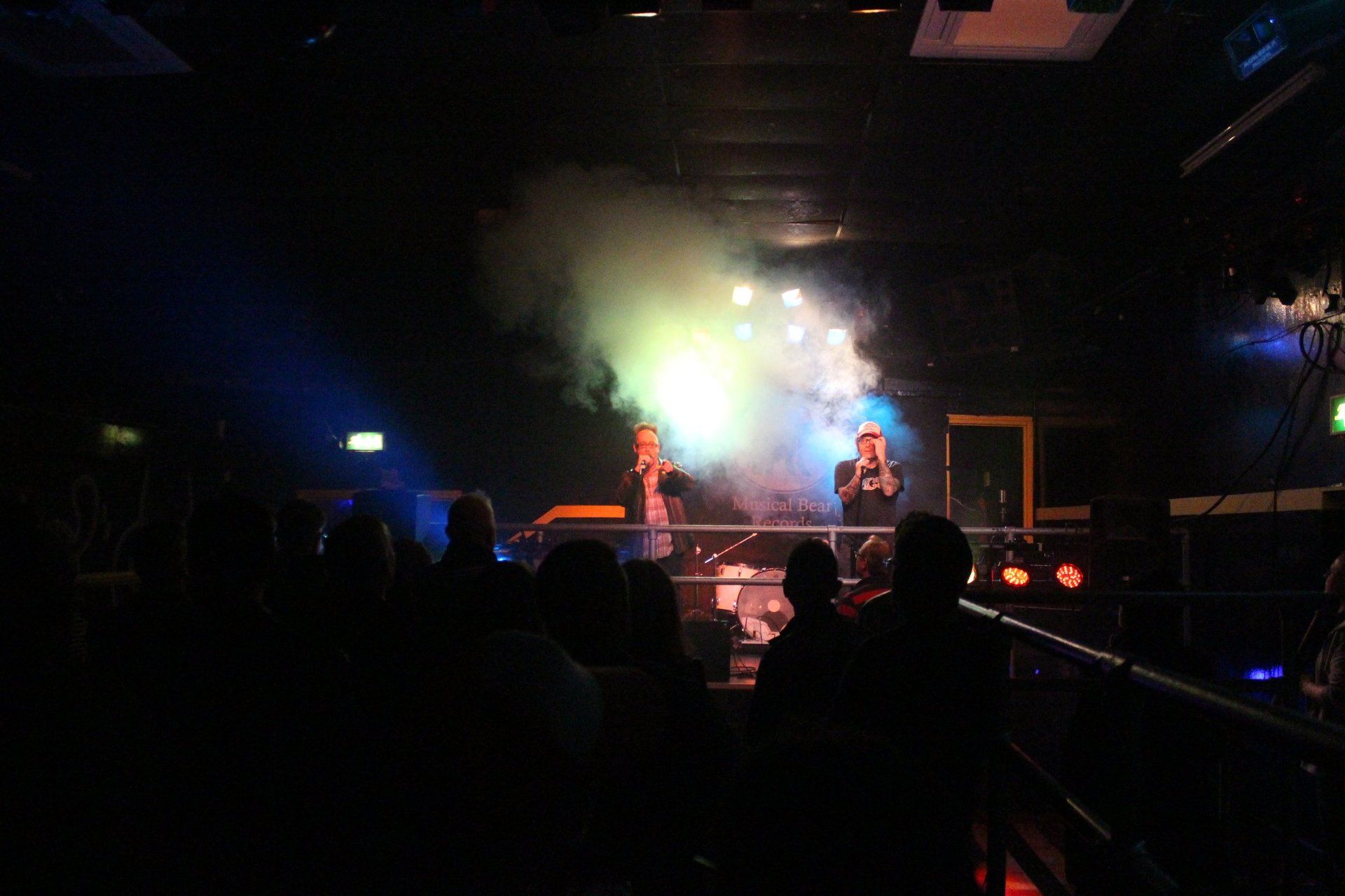 A group of people are standing in front of a stage in a dark room.