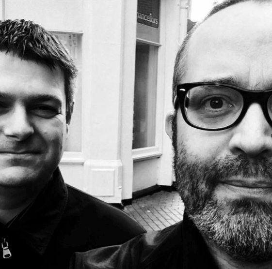 A man with glasses and a beard is standing next to another man