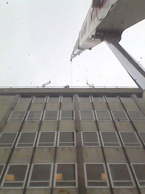 Crane arm over a tall building with many square windows, under an overcast sky.