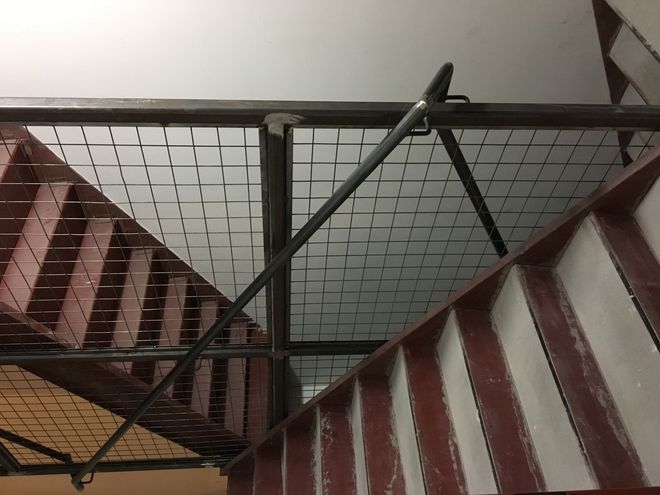 Steel staircase with wire mesh ceiling, red side rails, and a diagonal support beam.
