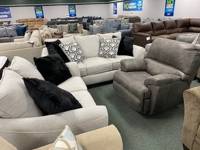Furniture store interior. Beige and black couches, gray recliner, many sofas in the background.