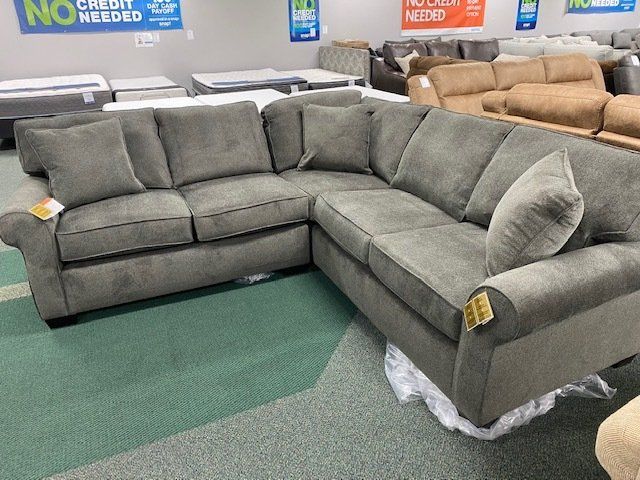 Gray sectional sofa on display in a furniture store, with green carpet and other furniture visible.