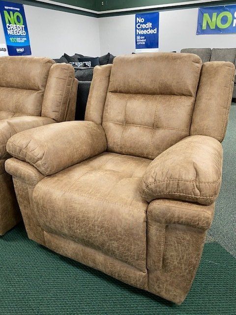 Tan, overstuffed recliner chair with tufted back in a furniture store setting.