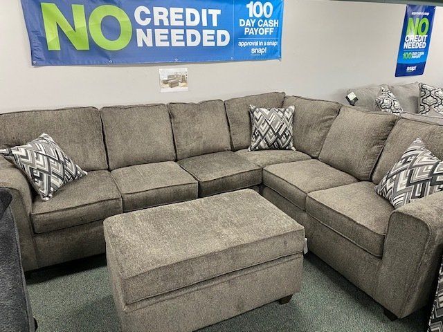 Gray sectional sofa and ottoman with patterned throw pillows. Sign above reads 