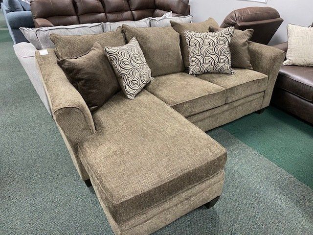 Brown sectional sofa with patterned pillows on display in a showroom setting.