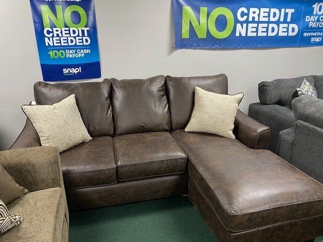 Brown leather sectional sofa with two beige pillows and a chaise lounge.