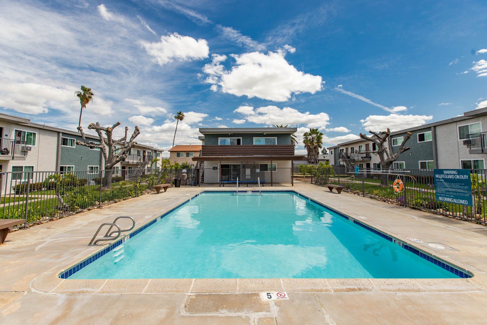 Outdoor swimming pool in a residential complex with apartment buildings and a blue sky backdrop