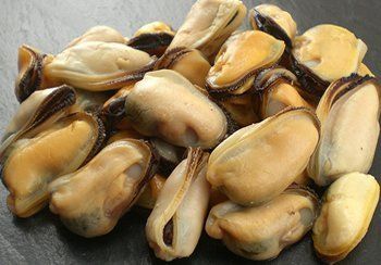 Cooked mussels piled on a dark surface, showing beige and orange flesh.