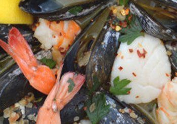 Close-up of mussels, shrimp, and scallops in a dish, garnished with parsley and red pepper flakes.