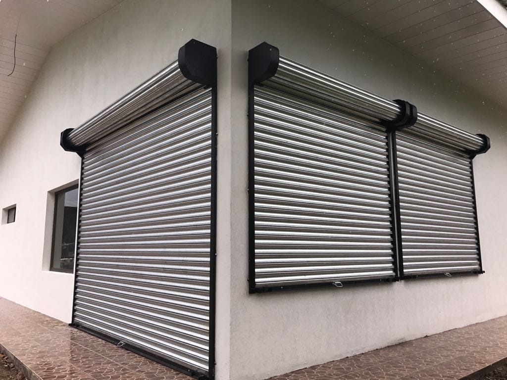 Persianas de seguridad de metal gris que cubren las ventanas de la fachada de un edificio.