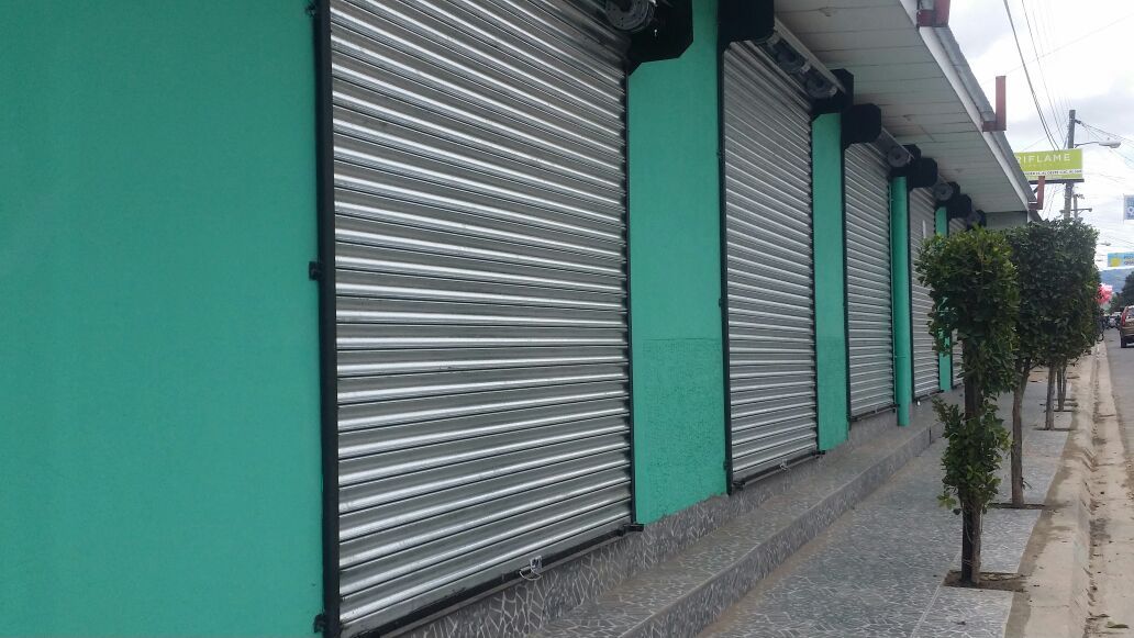 Persianas metálicas cerradas en la fachada turquesa de una tienda situada junto a la acera.