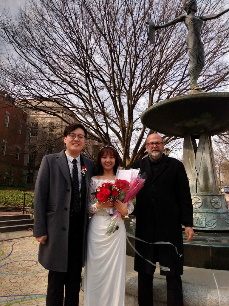 A bride and groom are posing for a picture in front of a fountain.