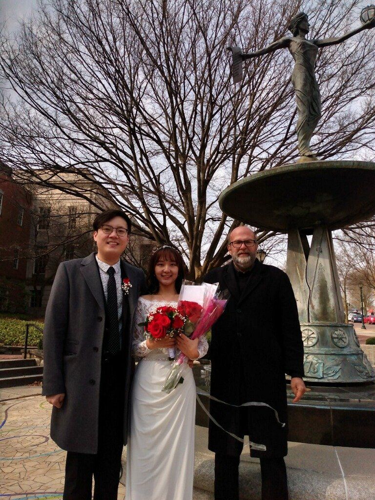 A bride and groom are posing for a picture in front of a fountain.