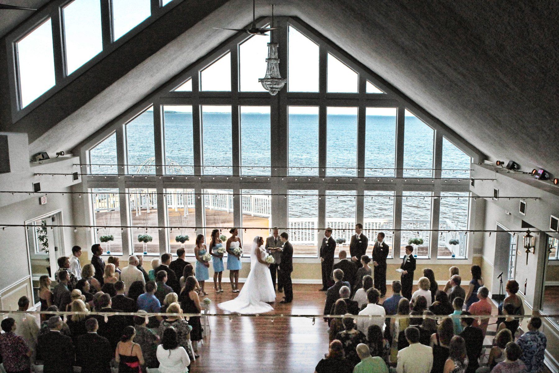 A bride and groom are getting married in front of a large window overlooking the ocean