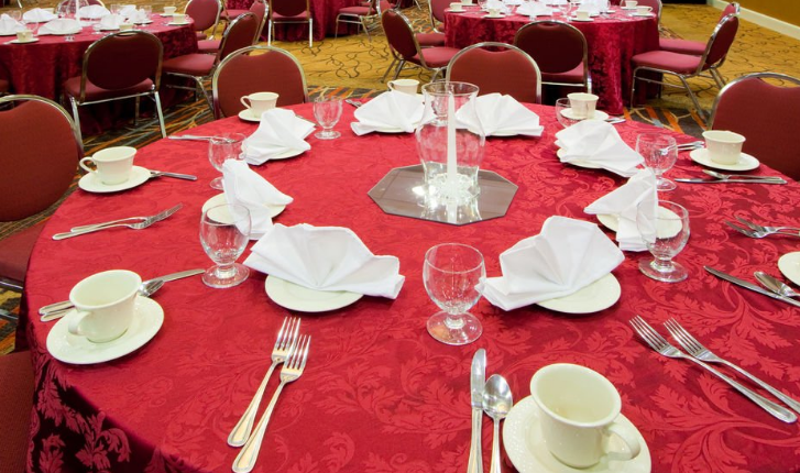 A round table with a red tablecloth and silverware is set for a banquet.